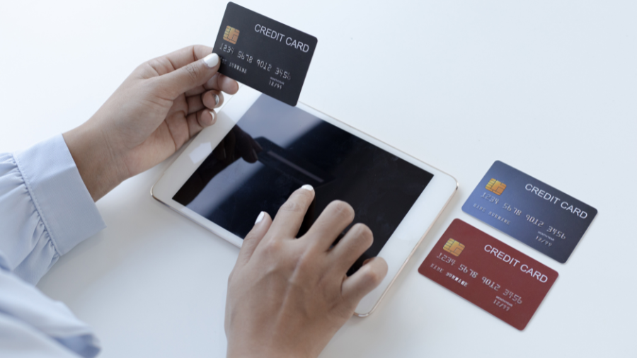 Person using a tablet and holding a credit card, with two other credit cards placed nearby.
