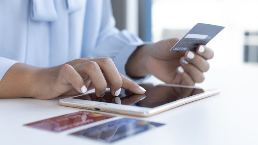 A person managing finances using a calculator and writing in a notebook, with coins, a pink piggy bank, and cash on the table.